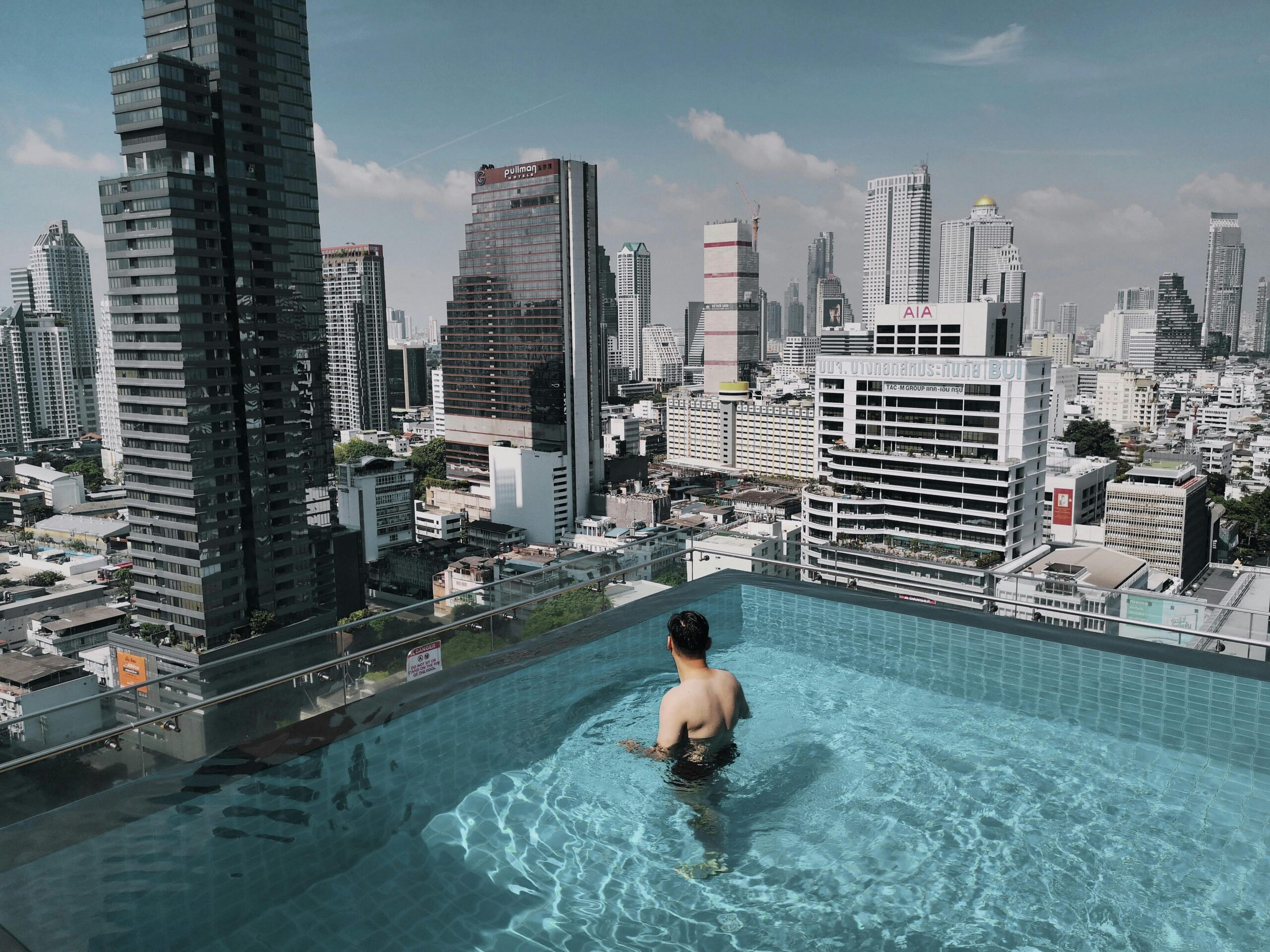 Man in rooftop pool with stunning view of Bangkok skyscrapers, Thailand.