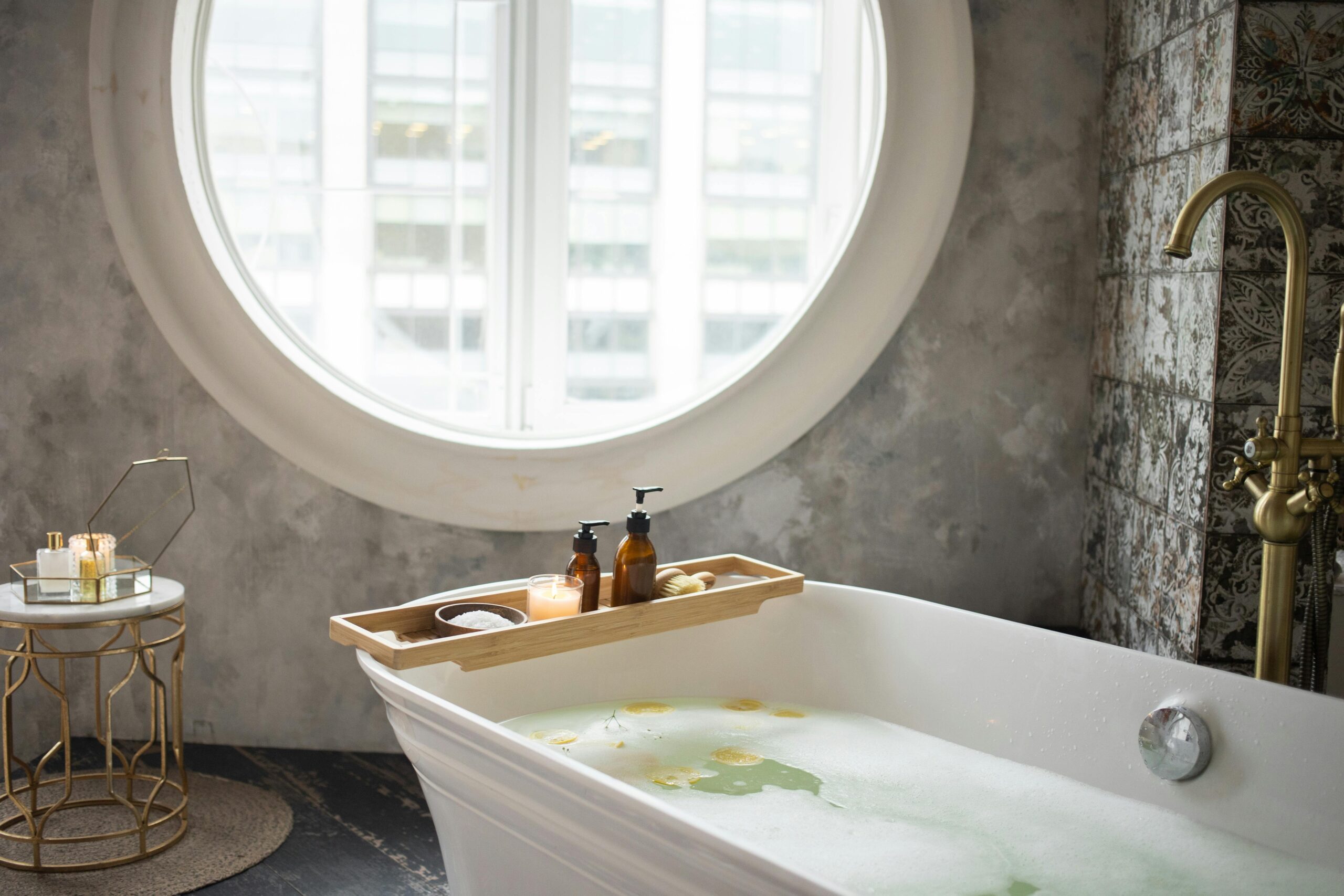 Elegant modern bathroom featuring a bathtub with spa essentials and a circular window.